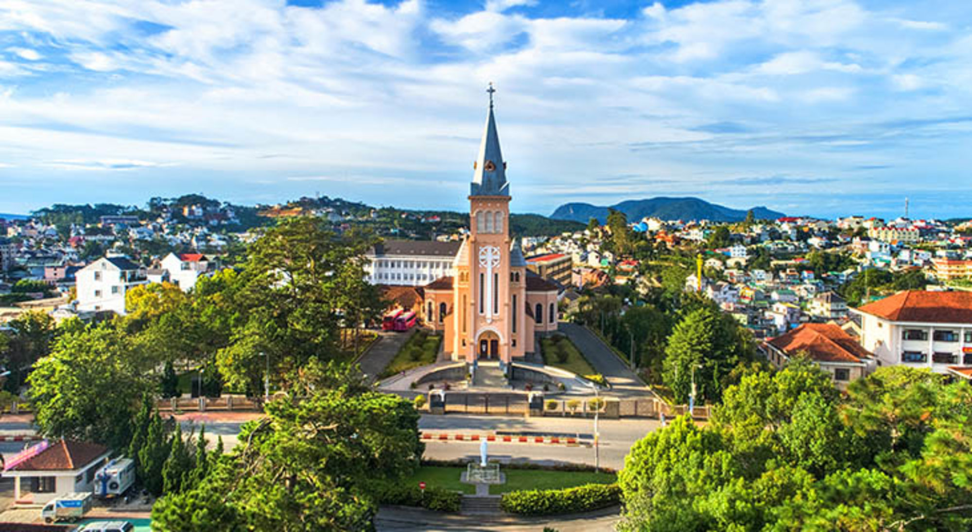 Da Lat Roze kathedraal met hoge torenspits in Da Lat, Vietnam, omringd door groen en stadshuisjes.