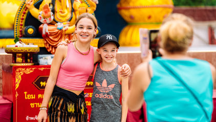 Twee kinderen poseren voor een Ganesha-beeld tijdens een familiereis in Thailand, terwijl iemand een foto maakt.