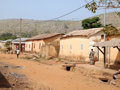 Straat in een dorp met lemen huizen en bewoners, met heuvels op de achtergrond in Ghana, Togo en Benin.
