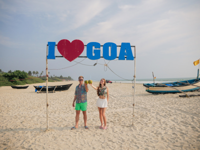 Reizigers proosten met kokosnoten onder het bord “I love Goa” op het strand van Goa, India.