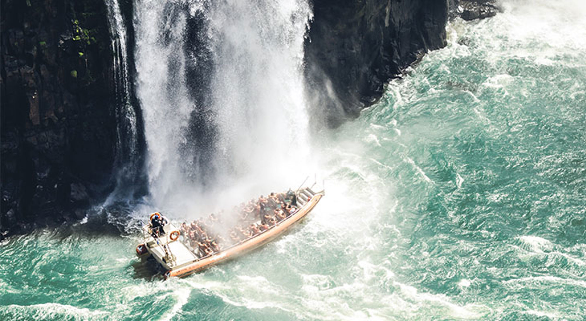Boottocht onder de Iguazú-watervallen in Argentinië, met passagiers in een rubberboot in opspattend water.