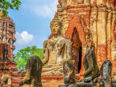 Thaise tempelruïne met stenen Boeddhabeeld tussen bomen.